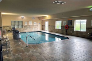 Una piscina interior con suelo de baldosas, señales de seguridad y una zona de estar cubierta.