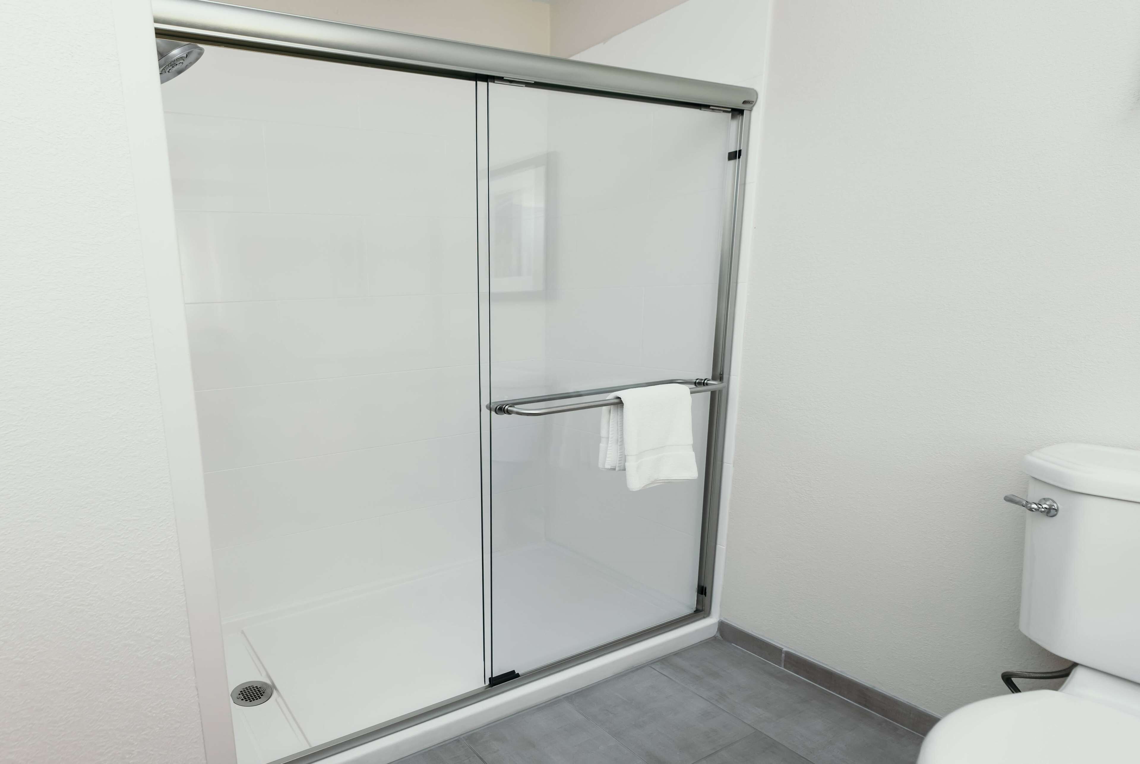 Une salle de bain moderne avec une douche à l’italienne en verre, des toilettes blanches et un sol carrelé de couleur grise.