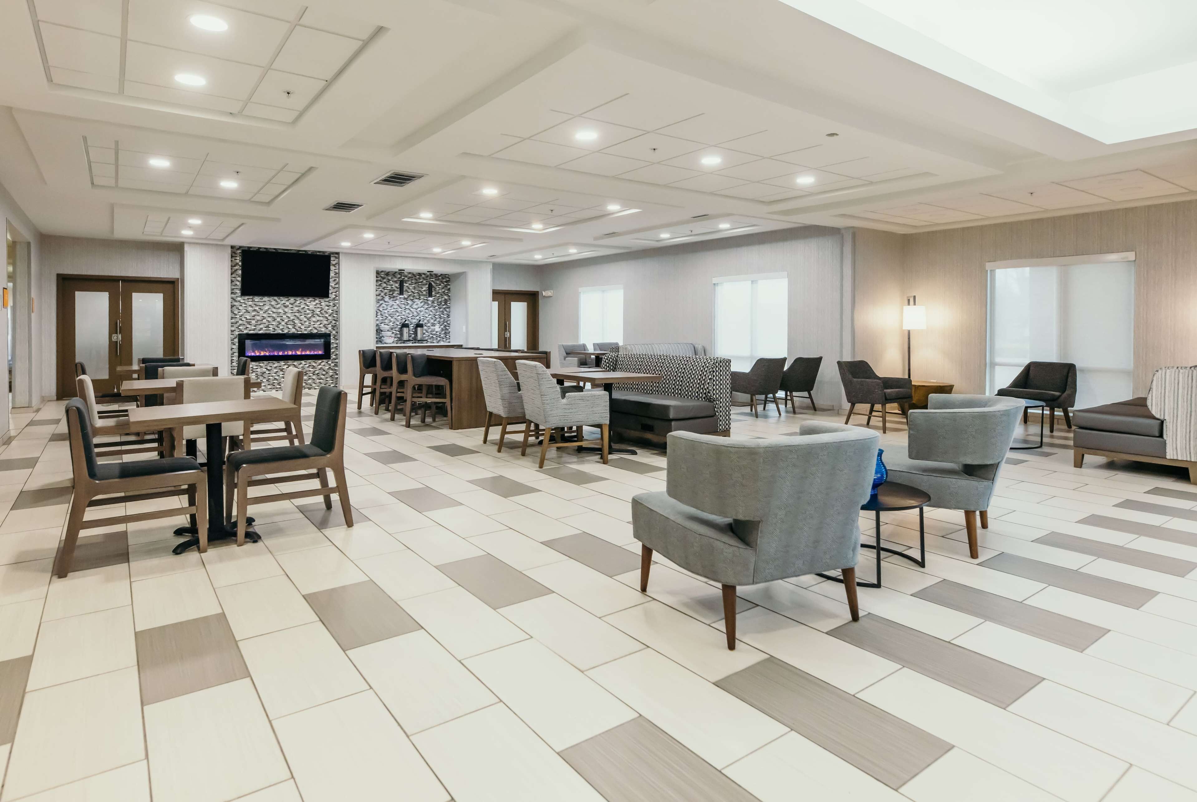 A spacious hotel lobby with multiple seating areas, a bar, and a large TV screen.