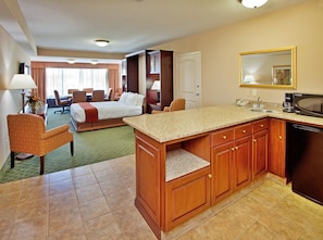 Habitación de hotel con cama, zona de estar, kitchenette y baño.