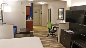 A hotel room with a bed, desk, chair, TV, and a small kitchenette area.