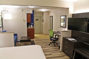 A hotel room with a bed, desk, chair, TV, and a small kitchenette area.