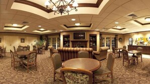 A spacious hotel lobby with a high ceiling, a central seating area with sofas and chairs, a fireplace, and a television mounted on the wall.