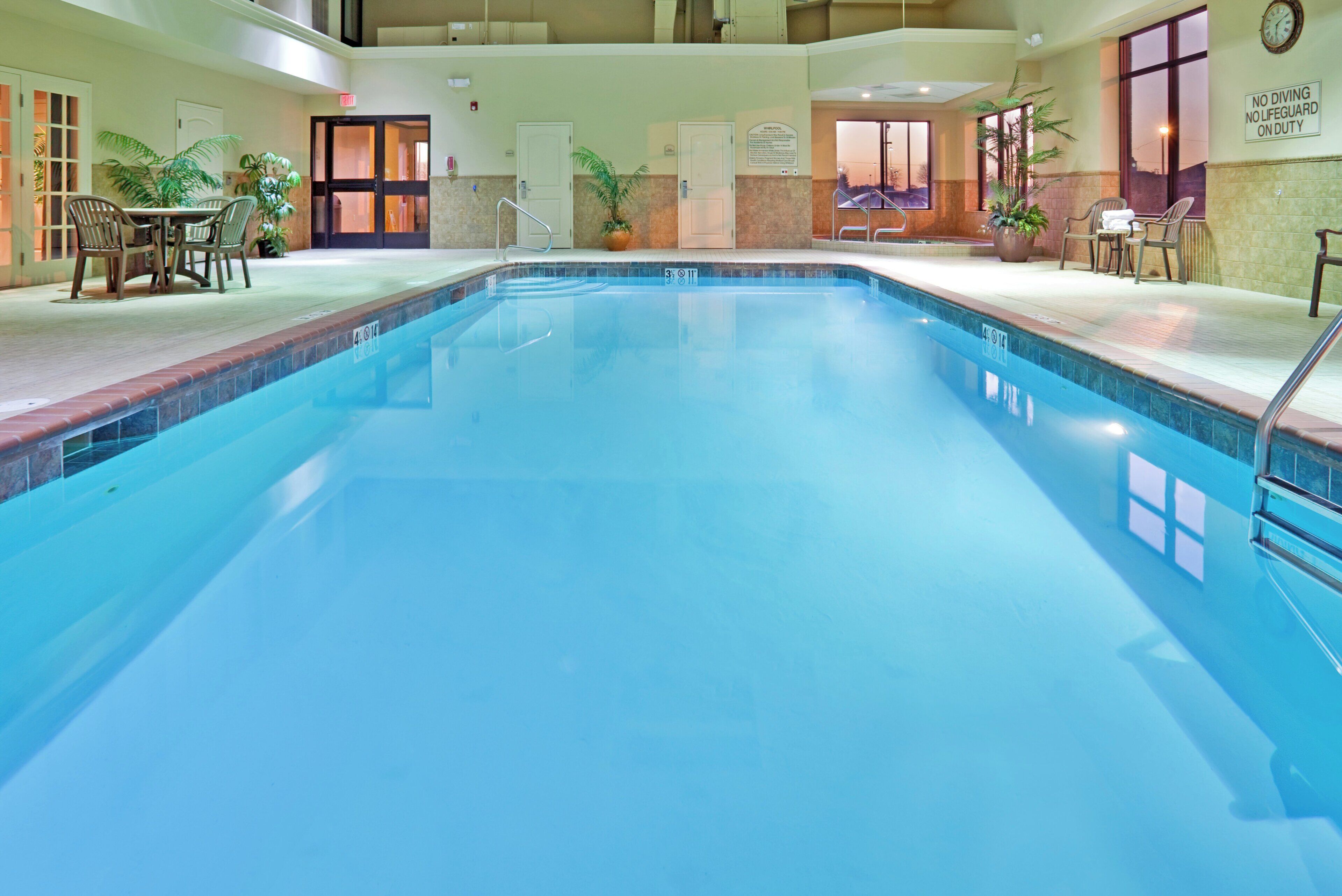An indoor swimming pool with clear water, surrounded by lounge chairs and a small table.
