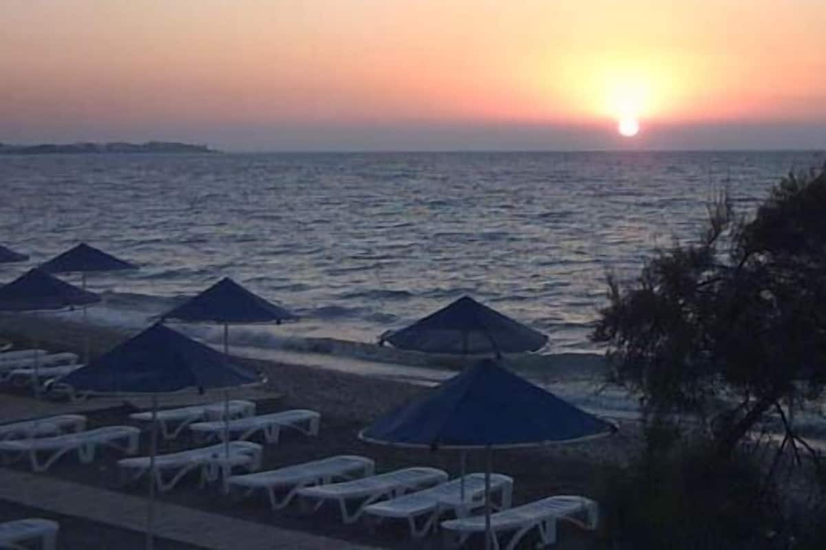 Une plage avec des chaises longues et des parasols, un coucher de soleil en arrière-plan et une mer calme.