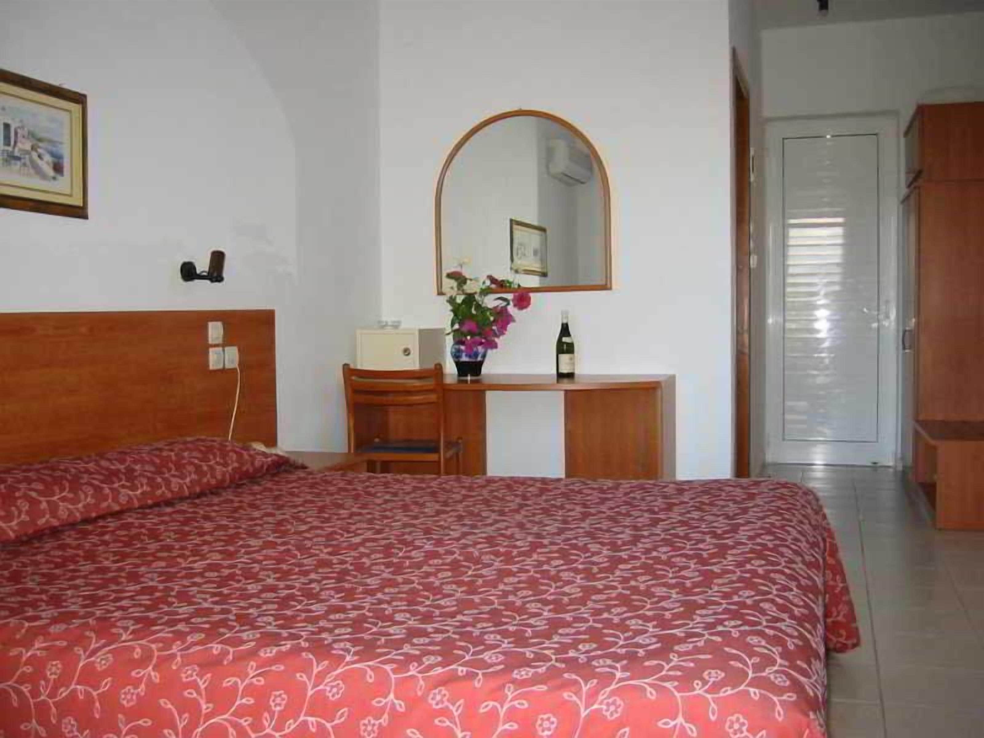 A bedroom with a bed, a desk, a chair, a mirror, and a wardrobe.
