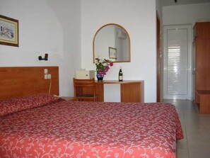 A bedroom with a bed, a desk, a chair, a mirror, and a wardrobe.