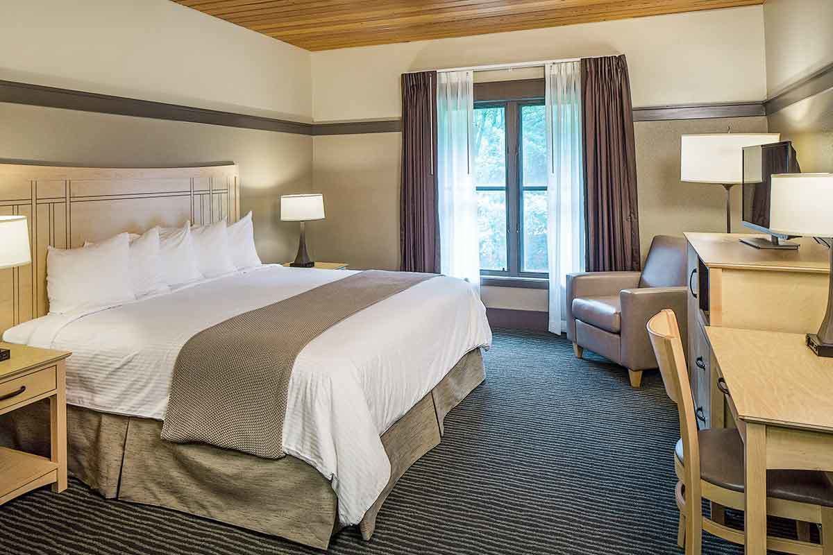 Une chambre d’hôtel avec un grand lit, un bureau, une chaise et une fenêtre avec des rideaux.