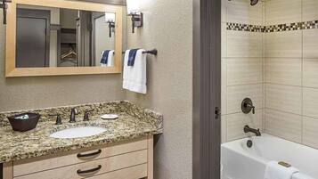 A bathroom with a granite countertop, two sinks, a mirror, and a bathtub.