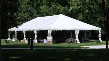 A white tent with a peaked roof, surrounded by a grassy area and trees.