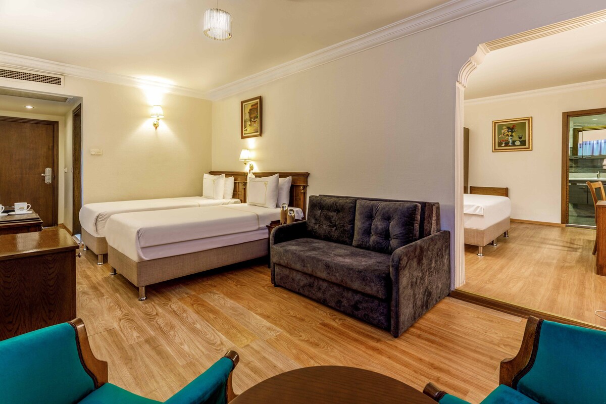 Ein Hotelzimmer mit Bett, einer Sitzecke, einem Esstisch und einem Spiegel.