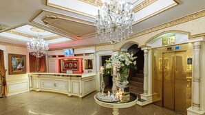 En lobby med receptionsdisk, lysekrone, elevator og trappe.