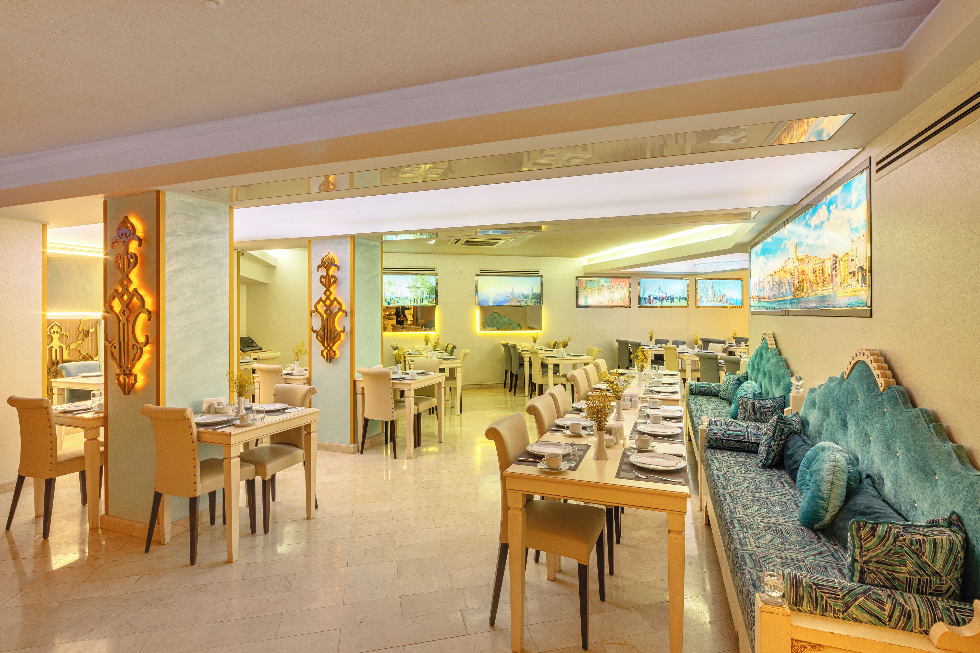 Un vaste espace dédié à la salle à manger, avec plusieurs tables et chaises, un long canapé agrémenté de coussins à motifs et un grand tableau accroché au mur.