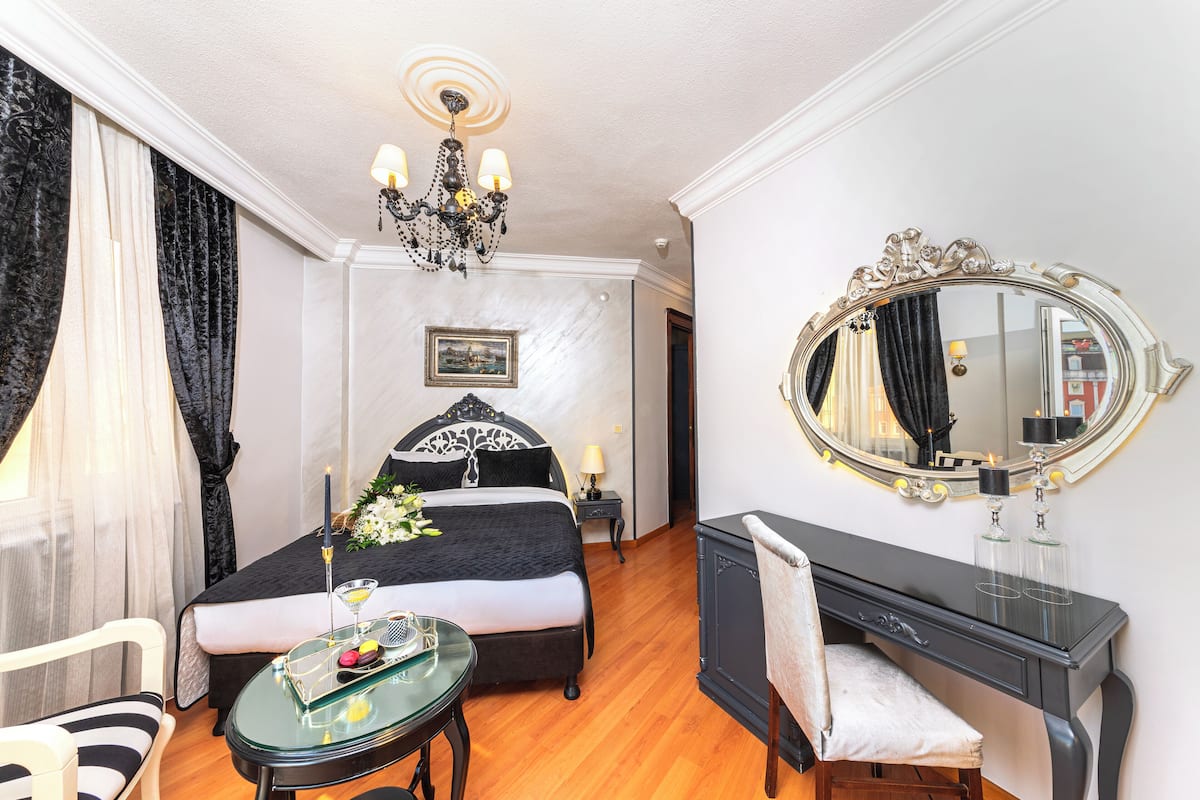 A hotel room with a bed, a desk, a chair, a round mirror, and a chandelier.