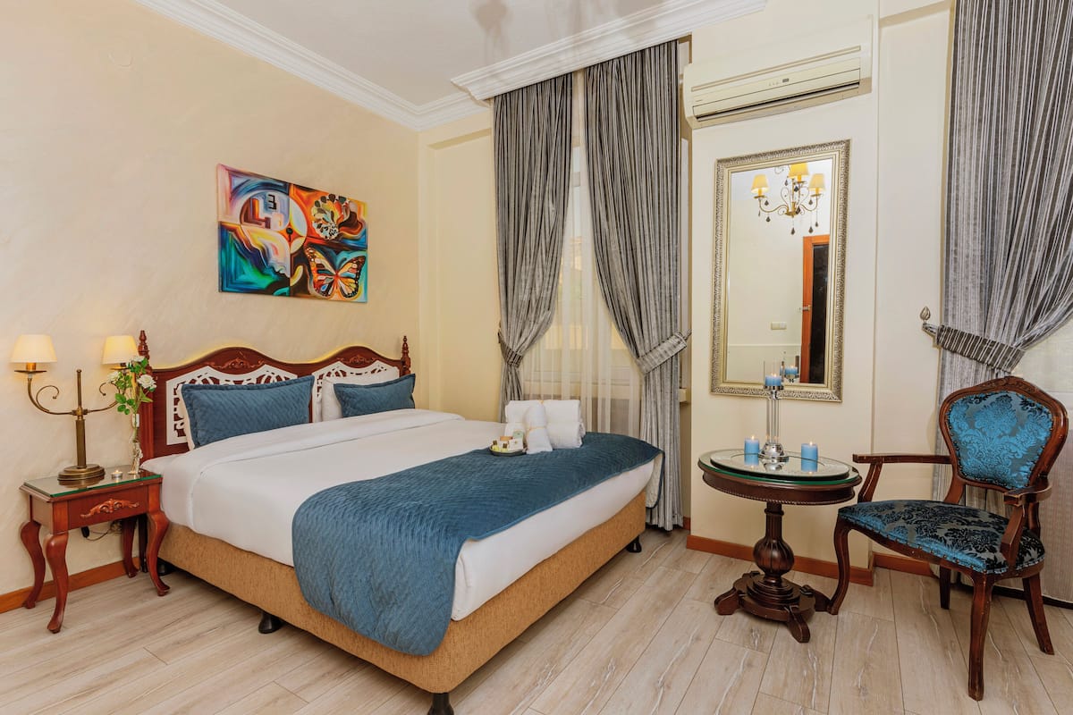 A hotel room with a large bed, a round table, a chair, a mirror, and a painting on the wall.