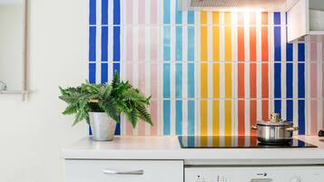 A kitchen with a white countertop, a stainless steel pot, a potted plant, and a wall with colorful vertical stripes.