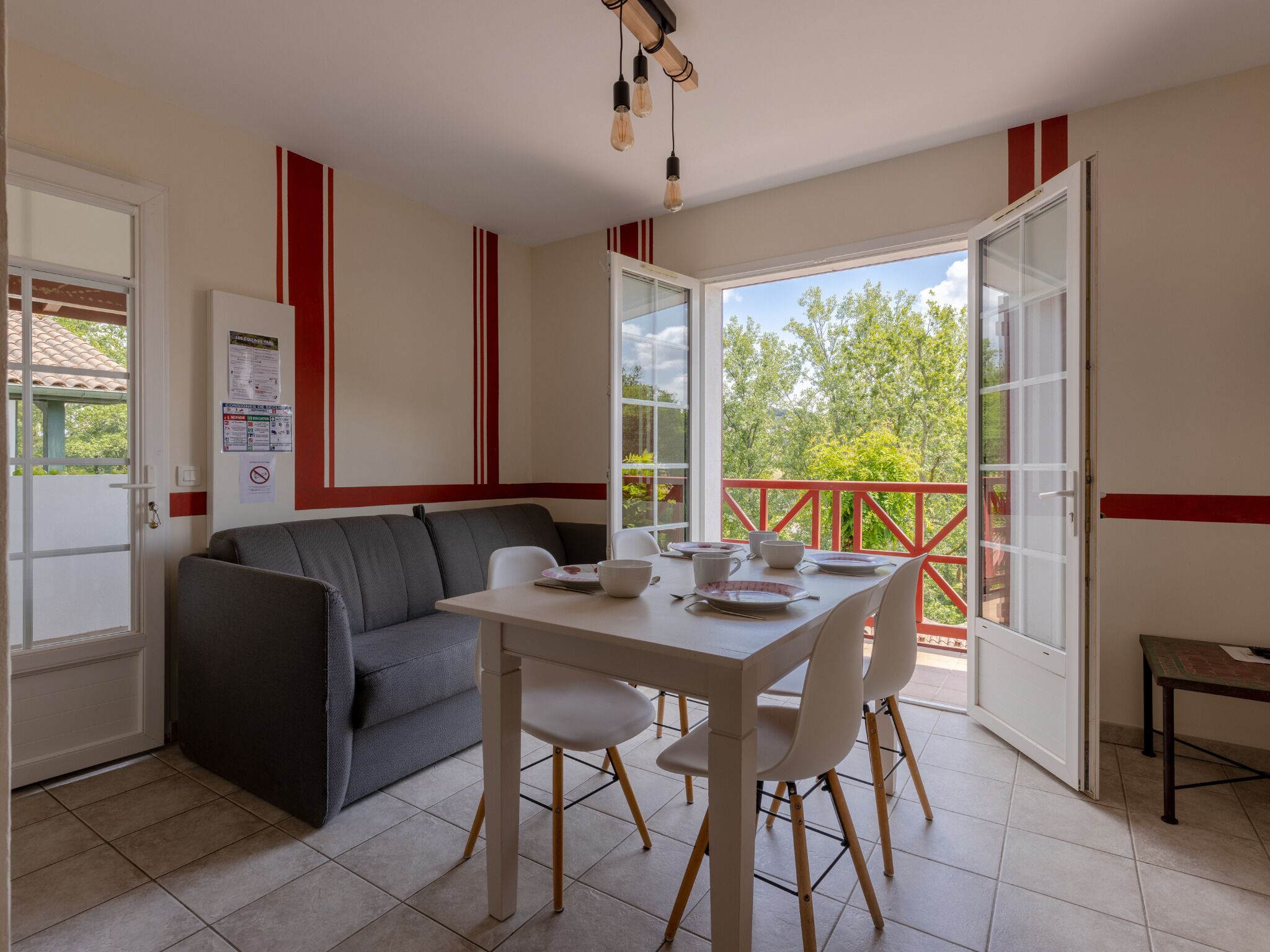 Un coin repas avec une table et des chaises, un canapé et un balcon doté d’une rambarde rouge.