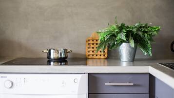 A kitchen with a stove, a pot, a potted plant, and a wooden utensil holder.