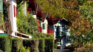 A row of traditional houses with red roofs and white walls, surrounded by lush greenery. - Les Collines Iduki (La Bastide-Clairence)