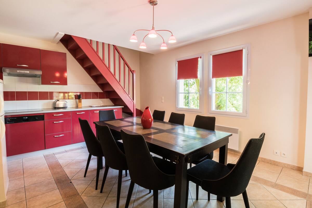 Una cocina moderna con armarios rojos, una mesa de comedor de madera y sillas negras.