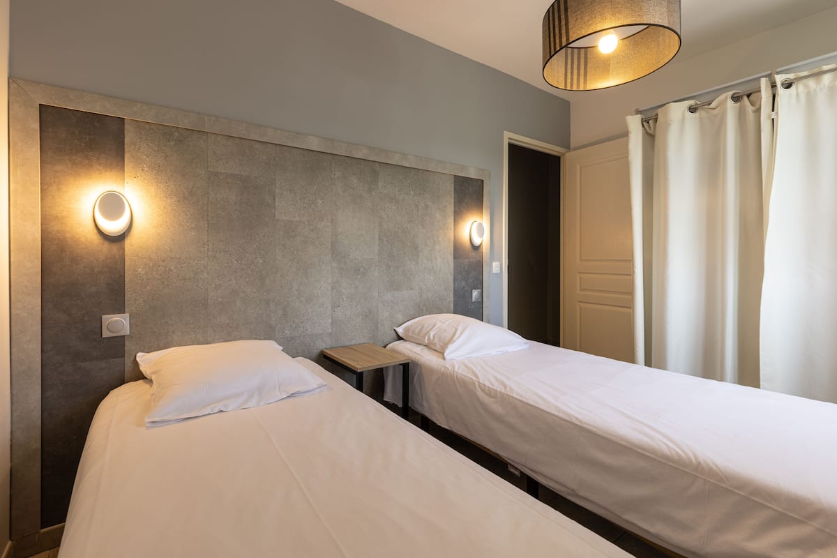 Habitación de hotel con dos camas individuales, una mesita de noche de madera y dos lámparas fijadas a la pared.