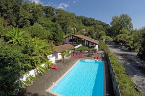 Une piscine entourée de verdure, avec un bâtiment et des chaises longues rouges en arrière-plan.