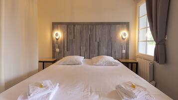 Een tweepersoonsbed met witte lakens, twee nachtkastjes, een houten hoofdbord en een raam met gordijnen.