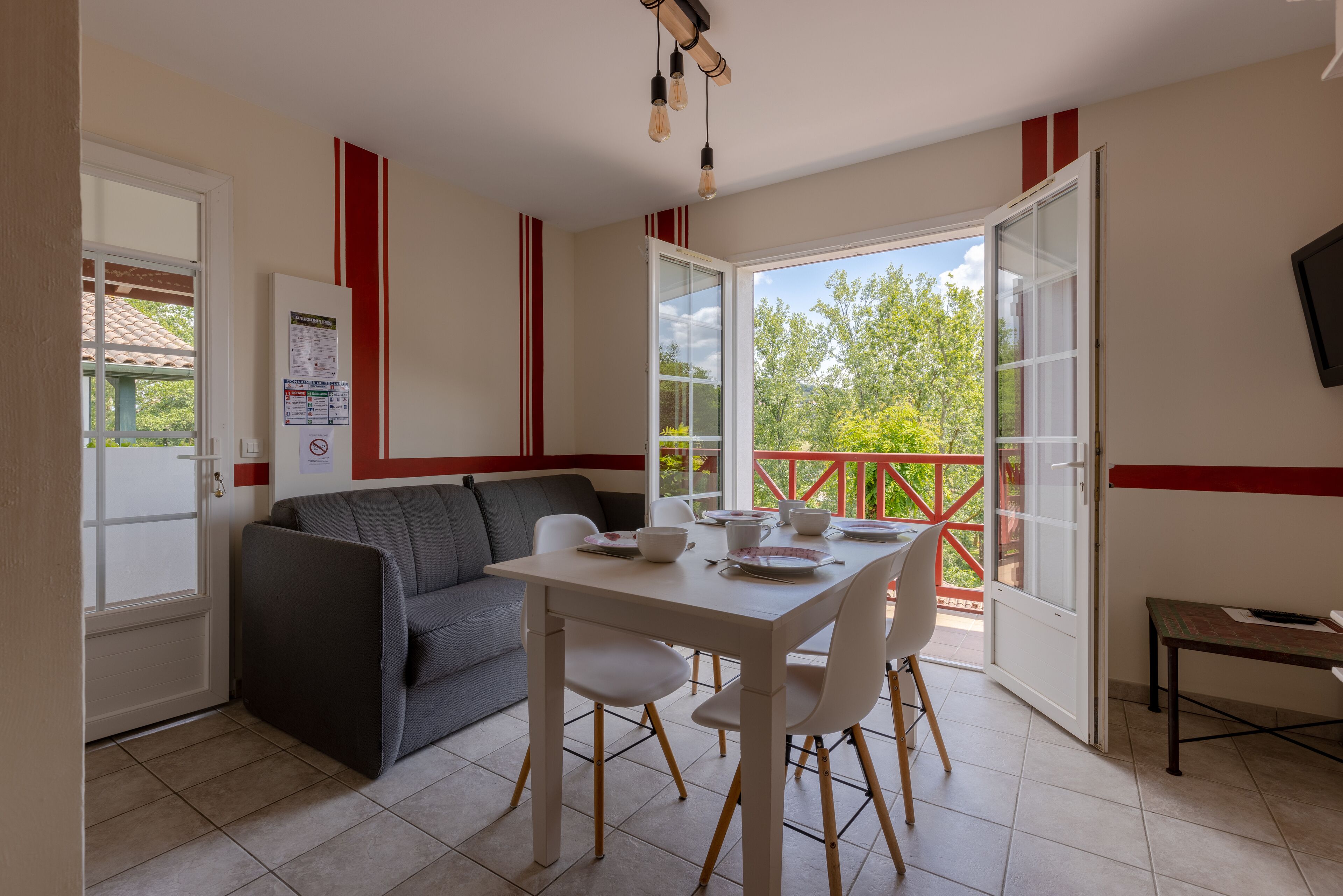 Een eethoek met een tafel en stoelen, een bank en een balkon met rode relingen.