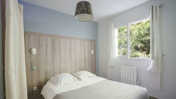 A bedroom with a bed, a window with curtains, a wooden headboard, and a ceiling light.