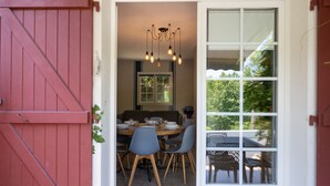 A dining area with a wooden table and chairs, a chandelier, and a view of greenery outside. - Les Collines Iduki (La Bastide-Clairence)