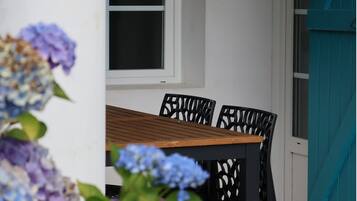Una mesa de madera con cuatro sillas, un ventanal y una puerta con contraventanas color turquesa.