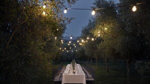 An outdoor dining area with a long table set for a meal, surrounded by chairs, and string lights overhead. - COMO Castello Del Nero (Barberino Tavarnelle)