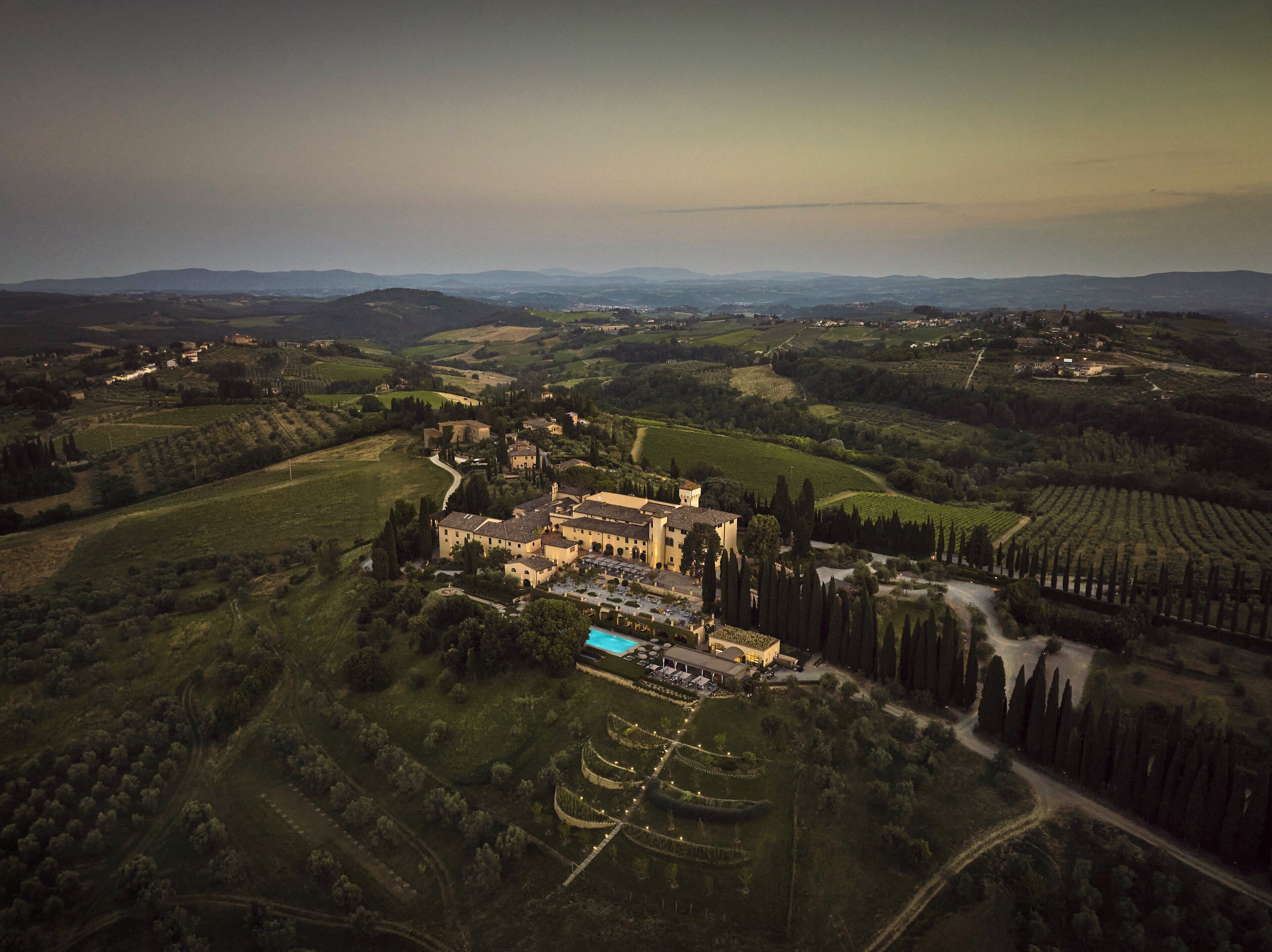 Vue aérienne d’un domaine historique comprenant plusieurs bâtiments, une piscine et des vignes aménagées en terrasses.