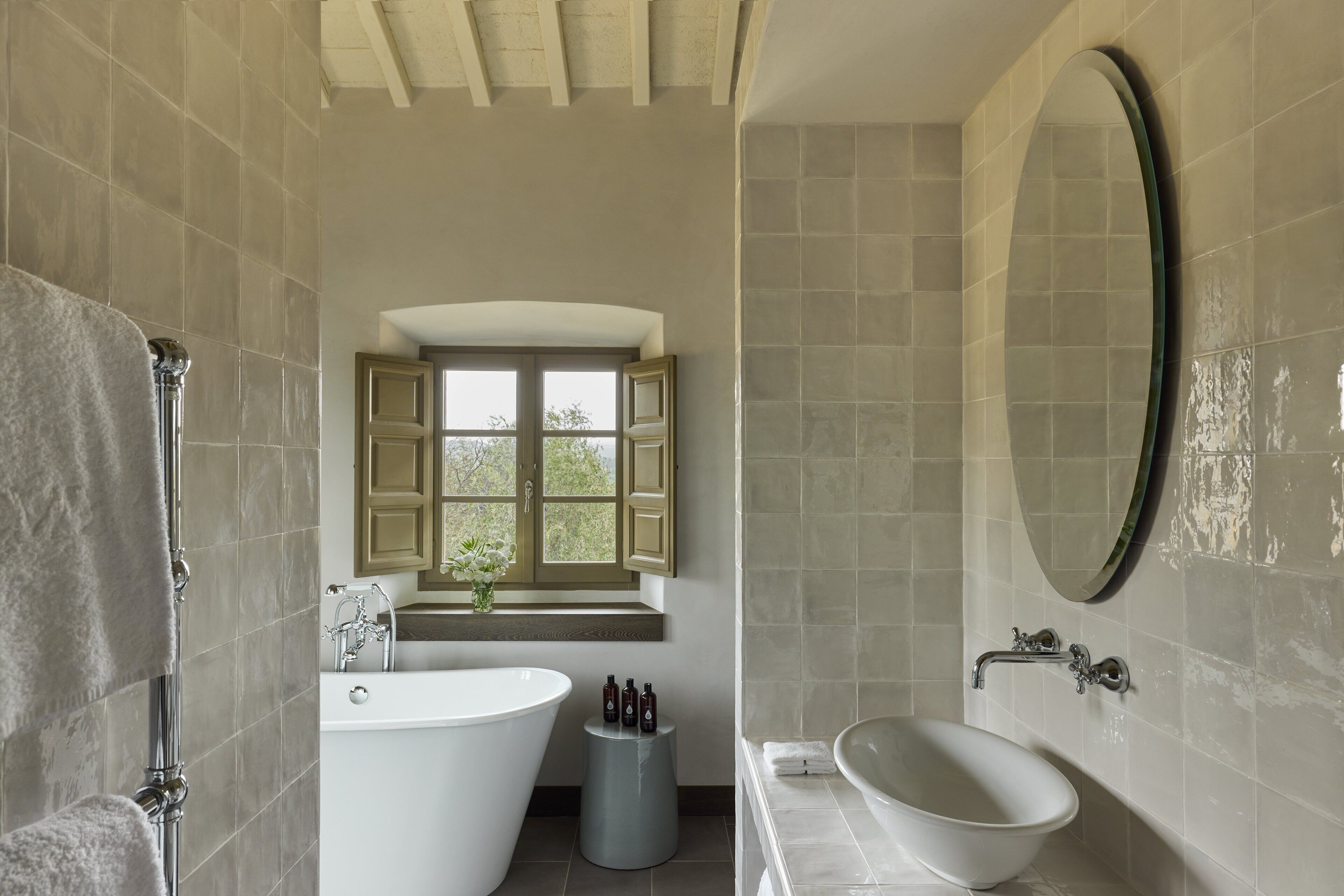 A bathroom with a freestanding bathtub, a large mirror, and a window with open shutters.