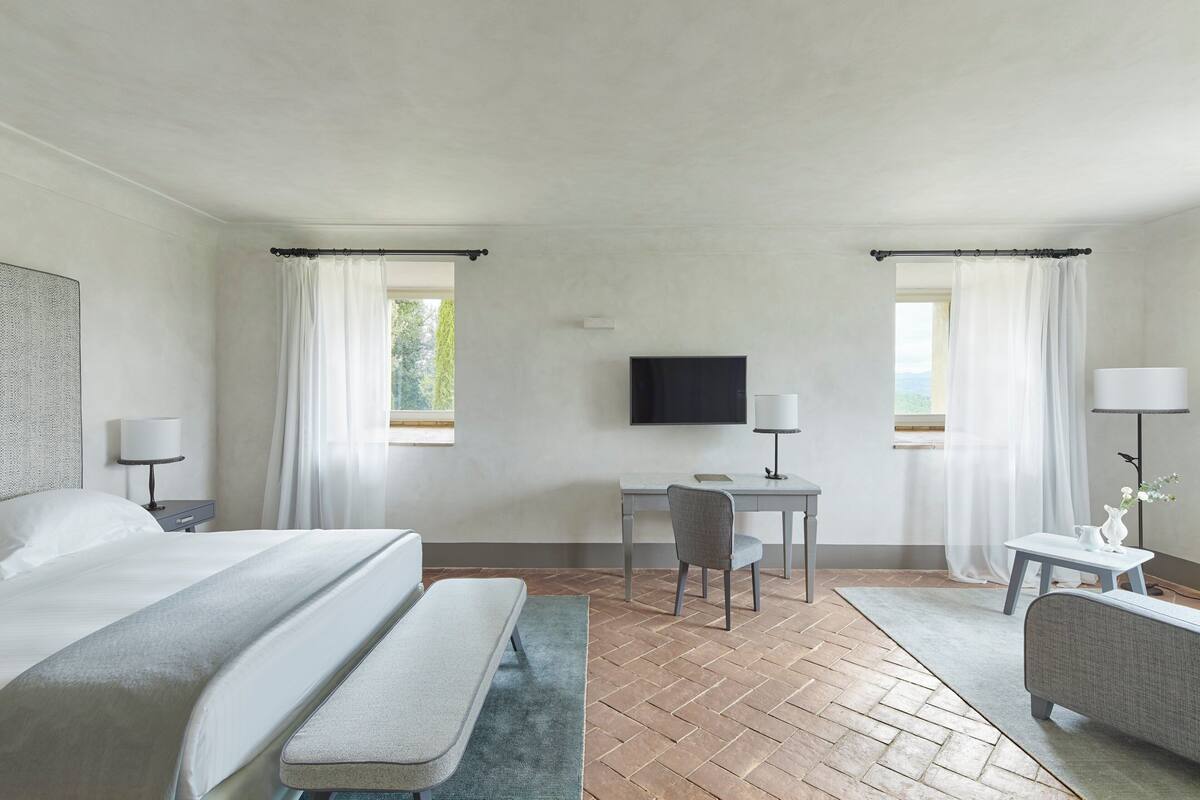 Una habitación de hotel con una cama, un escritorio, una silla, un banco y un televisor.