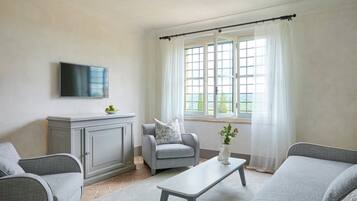 A living room with grey sofas, a flat-screen TV, a grey cabinet, and a window with white curtains.