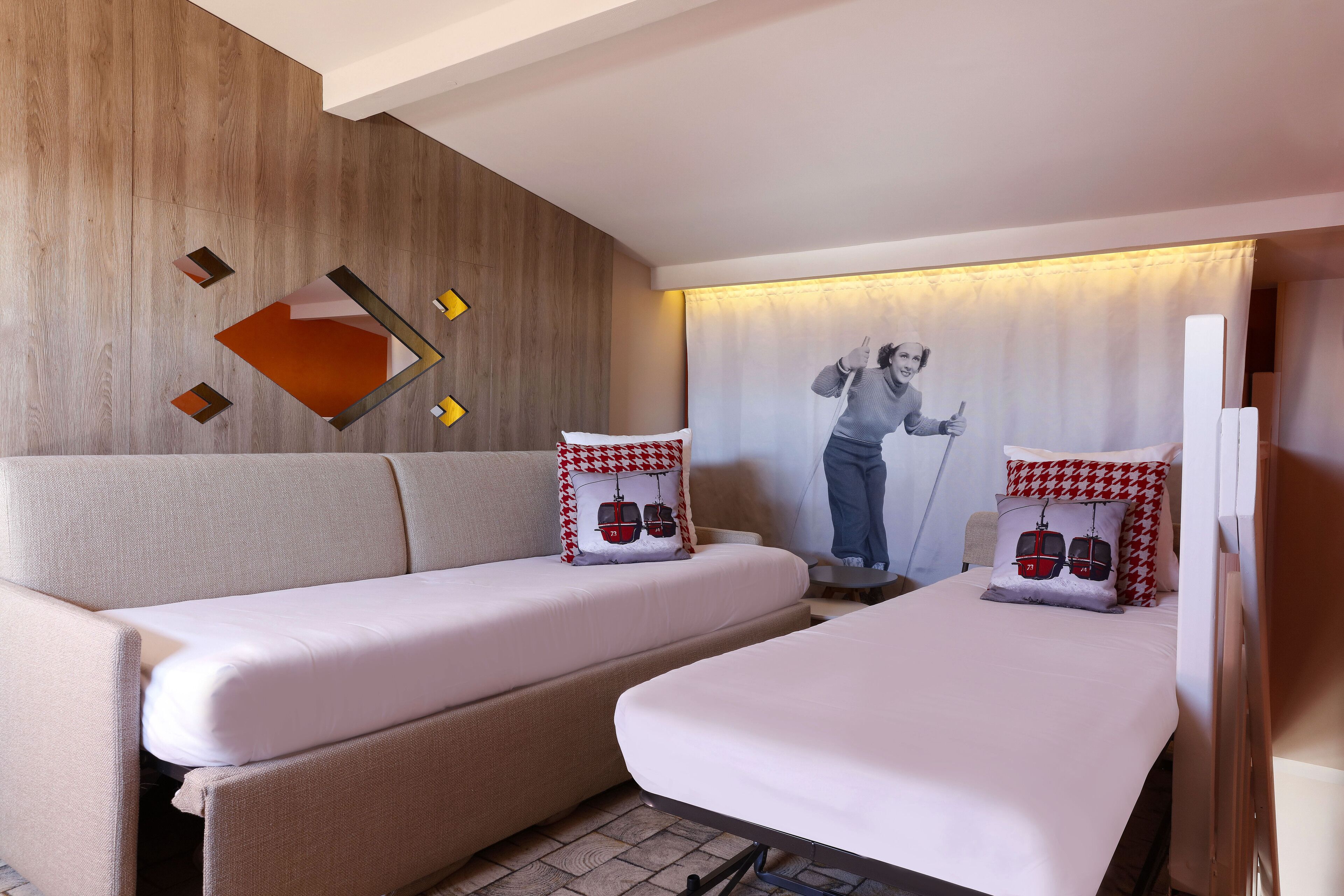A hotel room with a sofa bed, a smaller bed, and a wall-mounted TV.
