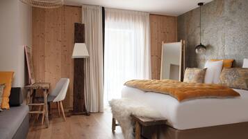 Habitación de hotel moderna con piso de madera, cama grande con un suave plaid blanco, escritorio con silla y una ventana amplia con cortinas traslúcidas.