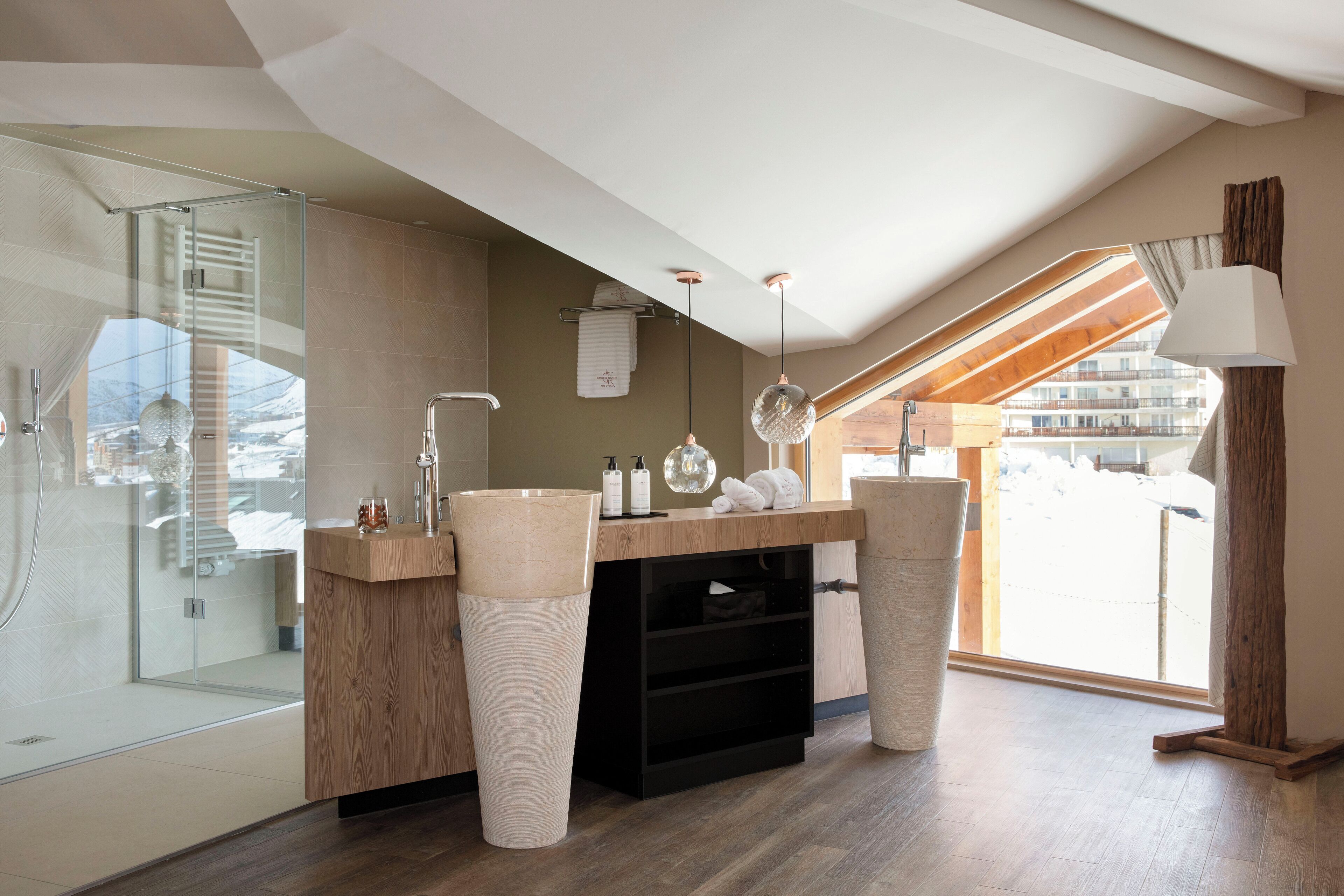 Ein modernes Badezimmer mit Duschabtrennung aus Glas, Holzwaschtisch und großem Fenster mit Blick ins Freie.