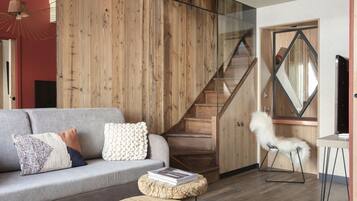 Un salon moderne avec un canapé gris, des murs recouverts de panneaux en bois, un escalier et une chaise blanche.