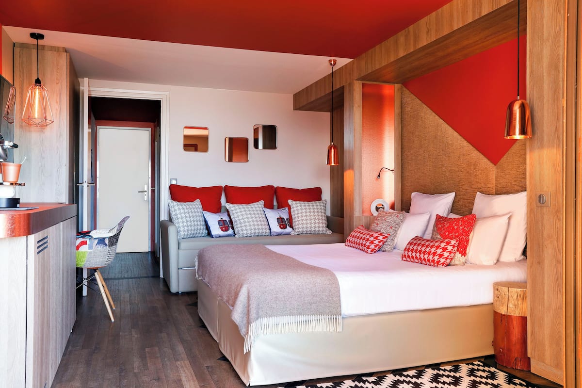 A modern bedroom with a large bed, a wooden headboard, and a red accent wall.