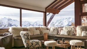 A cozy room with a large window overlooking snow-capped mountains, a plush sofa, a patterned armchair, and a rustic wooden coffee table. - Grandes Rousses Hotel & Spa (Huez)