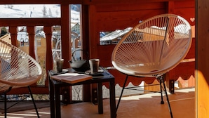 A balcony with two wicker chairs, a small table, and a view of snow-covered mountains. - Grandes Rousses Hotel & Spa (Huez)