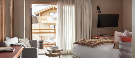 Ein Hotelzimmer mit Bett, Schreibtisch, Stuhl, Fernseher und Blick auf ein Holzhaus draußen.