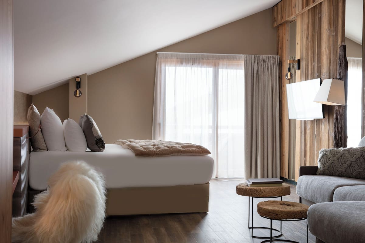 A modern bedroom with a large bed, a sofa, a small table, and a dog.