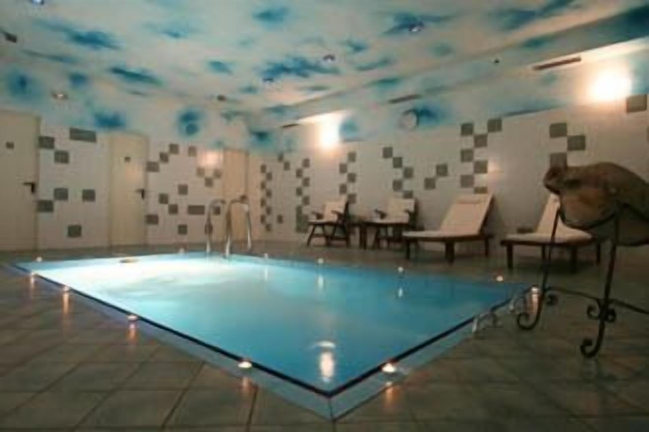 Una piscina con fondo de vidrio, rodeada de sillas de descanso y una pared con diseño geométrico.