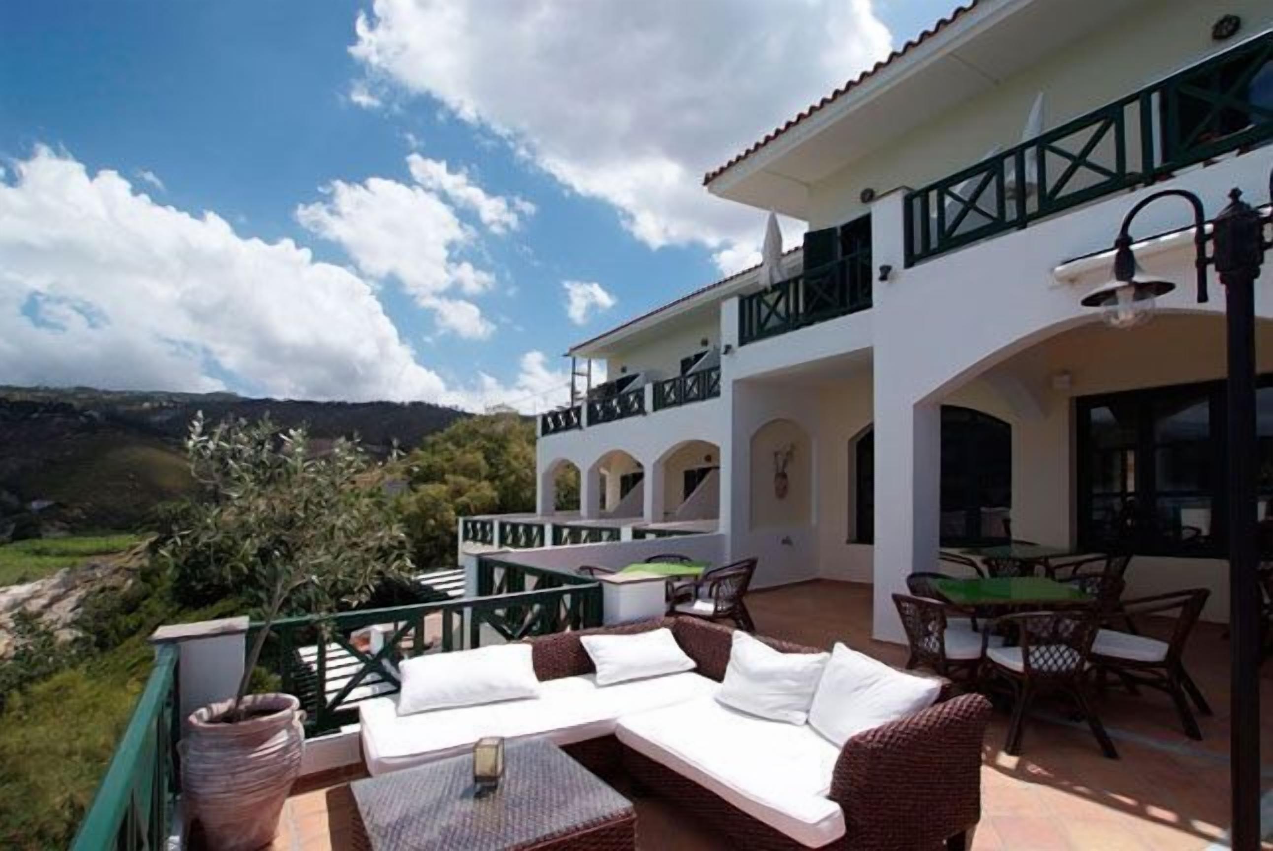 A spacious outdoor patio with a white sofa, wicker chairs, and a dining table.