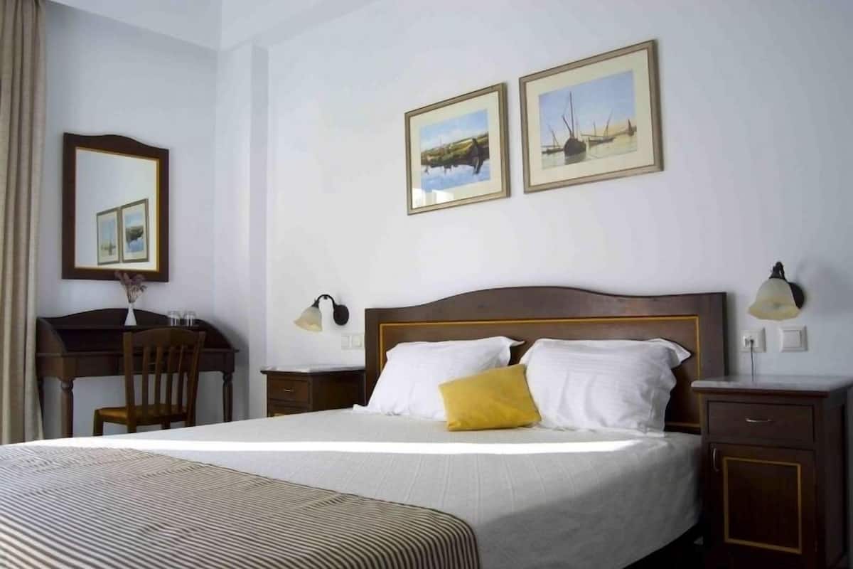 A hotel room with a large bed, a desk, a chair, and two framed pictures on the wall.