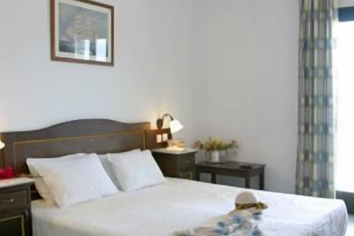 A hotel room with a large bed, a nightstand, a lamp, and a framed picture on the wall.