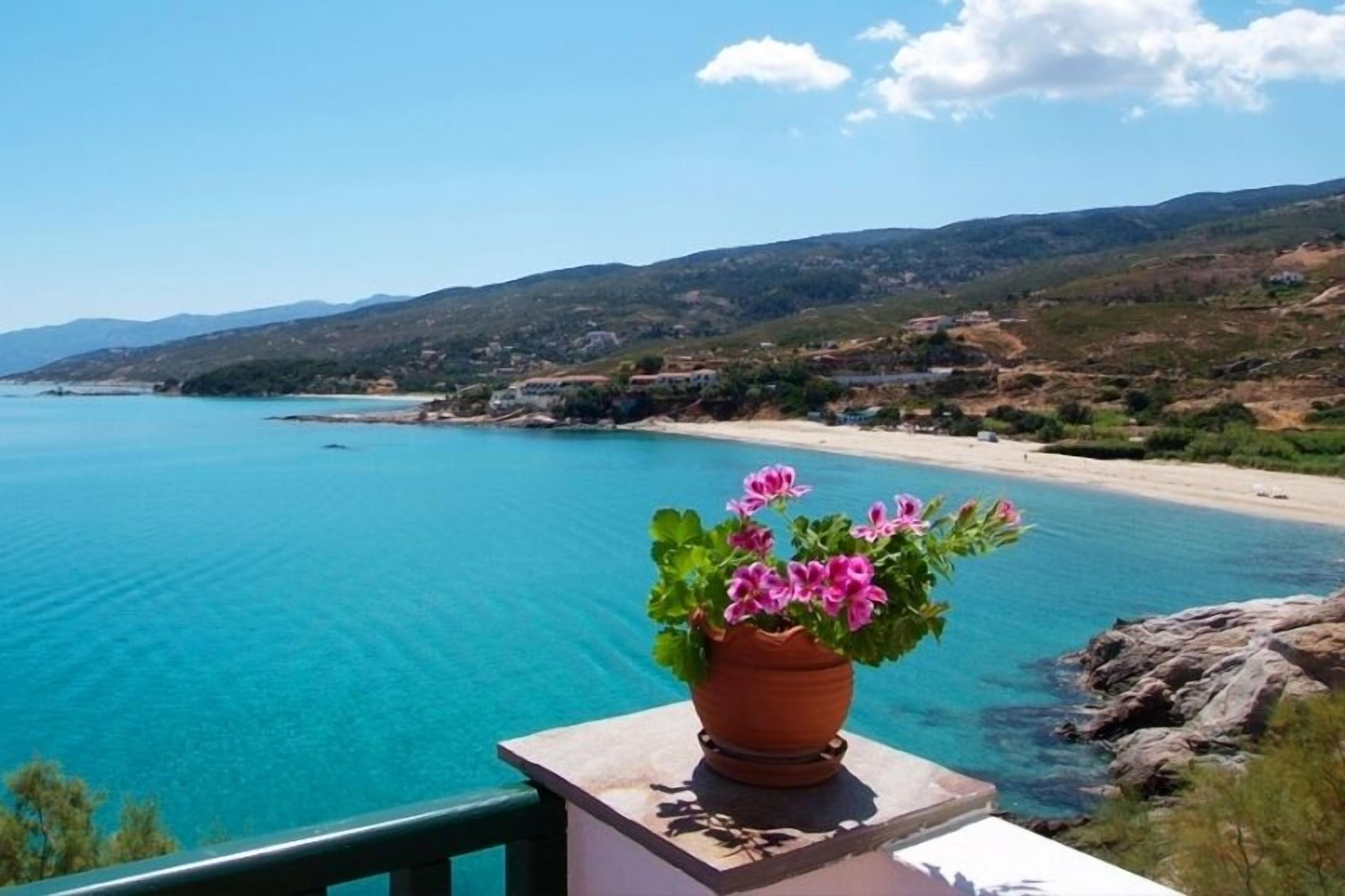 Vista costera con un mar azul y transparente, una playa de arena y montañas al fondo.